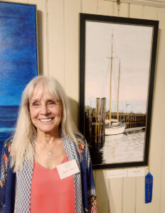 Smiling woman at art exhibit with sailboat painting